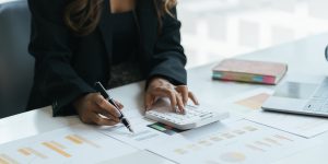 Businesswoman analyzing financial charts and using a calculator for budgeting and financial planning in an office