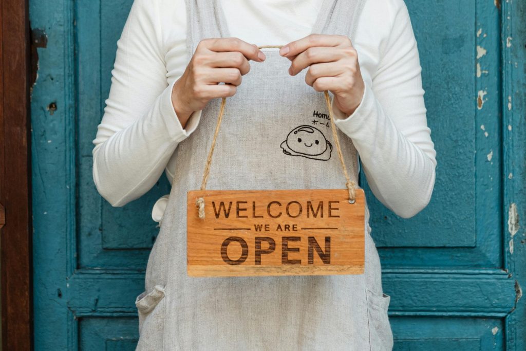 Small business owner holding a wooden sign that says 'Welcome, We Are Open".