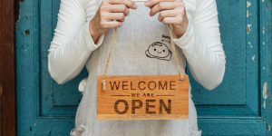 Small business owner holding a wooden sign that says 'Welcome, We Are Open